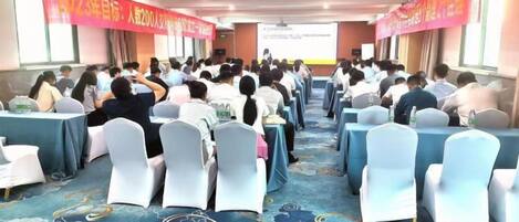 A conference room with rows of tables and chairs, a carpeted floor, and a presentation screen at the front.