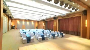 Una sala conferenze con file di sedie bianche, un palco e un grande sipario come sfondo.