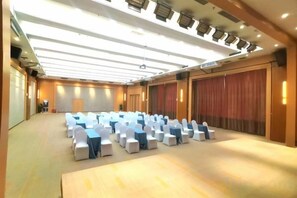 Un salón de conferencias con filas de sillas blancas, un escenario y un gran telón de fondo.