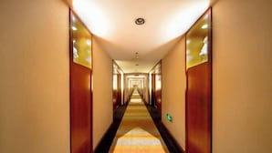 Un largo y estrecho pasillo de hotel con piso alfombrado y paneles de madera en las paredes.