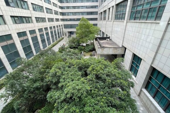 A multi-story building with a central courtyard featuring a large tree and various shrubs. - shi bo hotel (Zhengzhou)