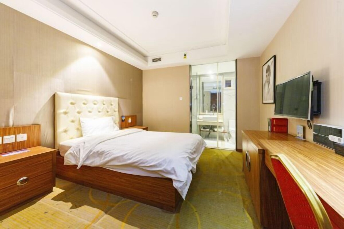 A hotel room with a bed, bedside tables, a TV, and a desk.