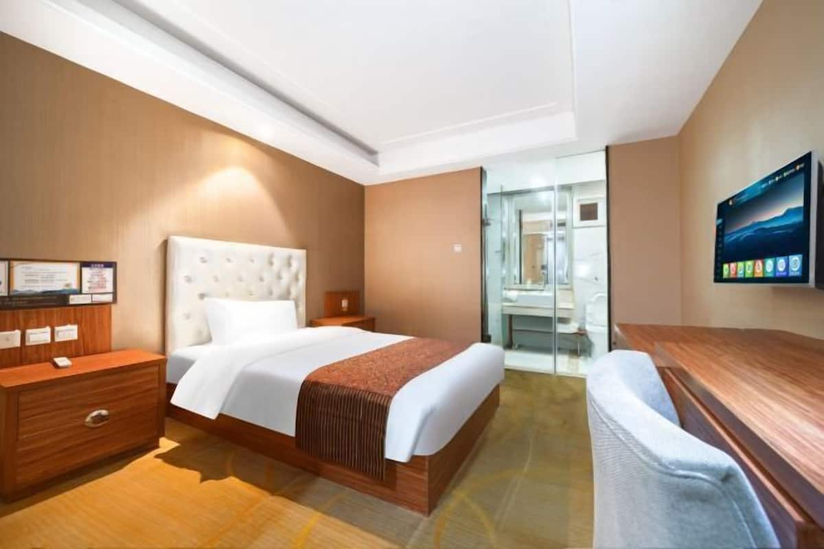 Una habitación de hotel con cama, escritorio, silla, espejo y televisor.