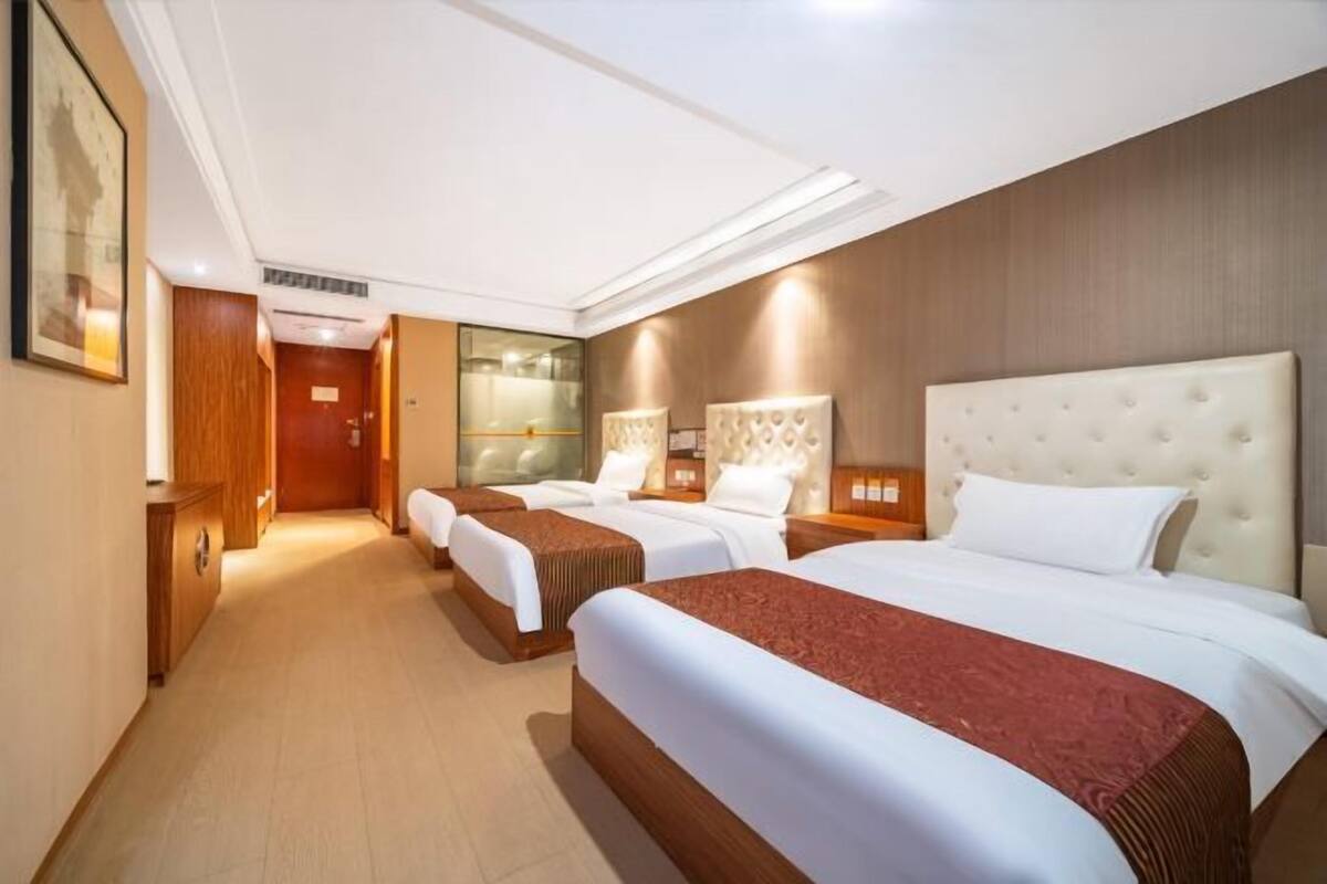 Habitación de hotel con tres camas, piso de madera y un espejo grande.