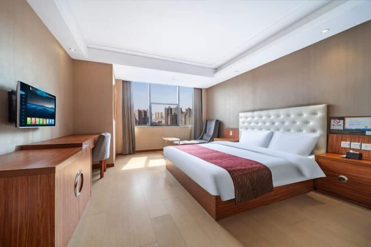 Habitación de hotel con cama, escritorio, silla, televisor y ventana con vista a la ciudad.