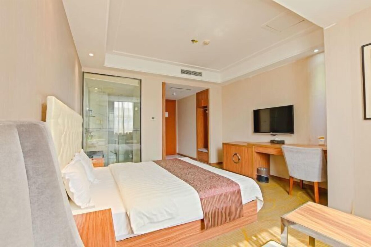 A hotel room with a bed, a desk, a television, and a glass partition.