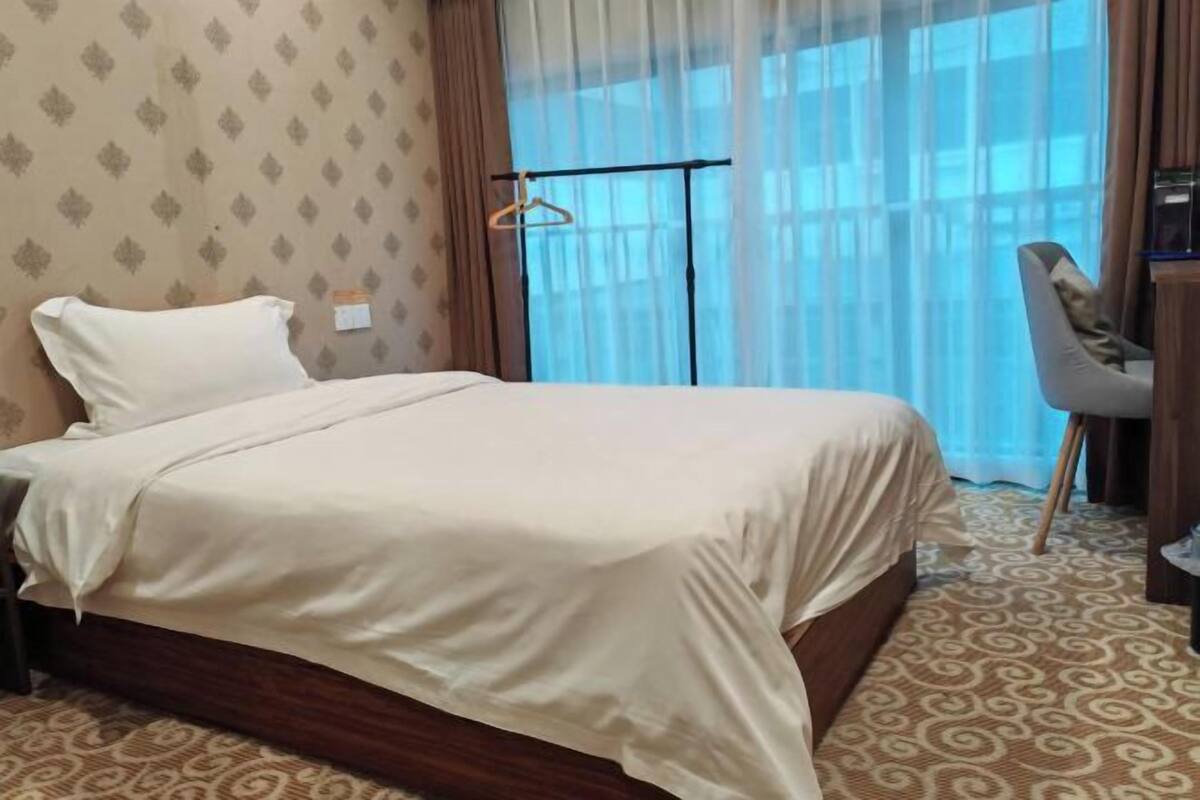 Habitación de hotel con cama, escritorio, silla y ventana con cortinas.