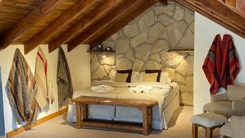 A bedroom with a stone wall, wooden ceiling beams, a bed, a bench, and a chair.