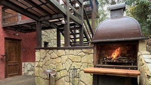 Un barbecue en pierre installé à l’extérieur, doté d’une cheminée en métal, d’une table en bois et d’un tabouret en métal.