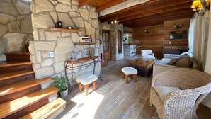 Un intérieur rustique avec des murs en pierre, des poutres en bois, une cheminée en pierre, un canapé et un fauteuil en osier.