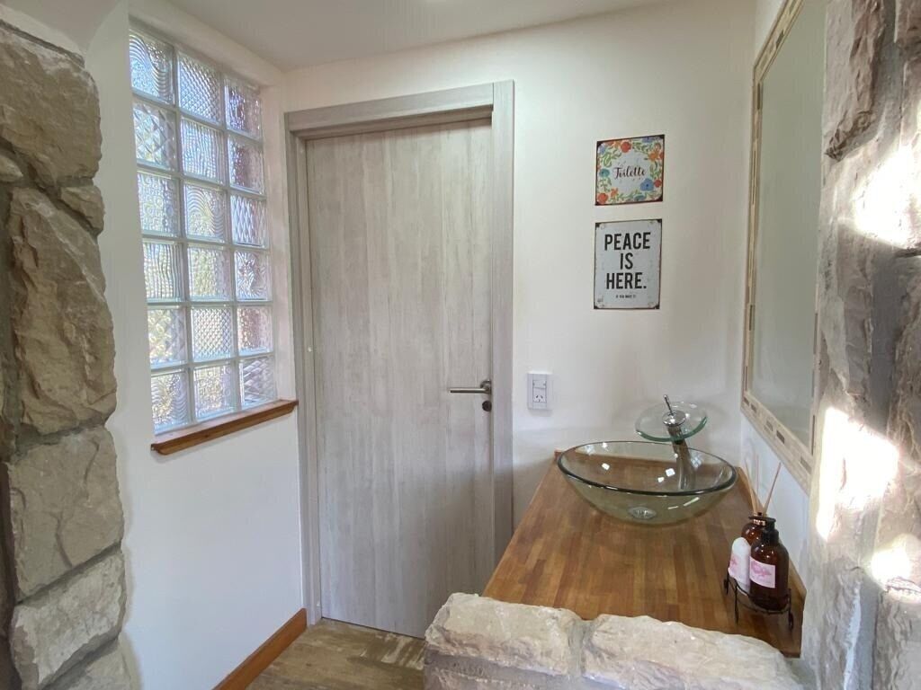 A hallway with a wooden door, a glass bowl sink, and a 'Peace is Here' sign.