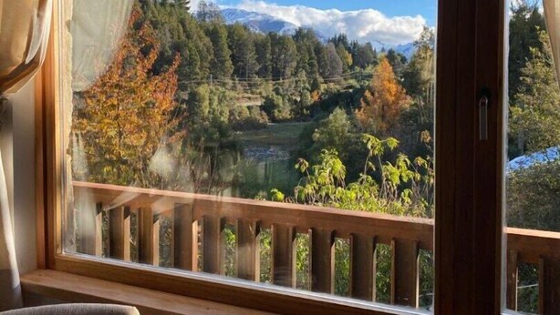 Une pièce dotée d’une grande fenêtre donnant sur un paysage magnifique : un lac entouré d’arbres et de montagnes.
