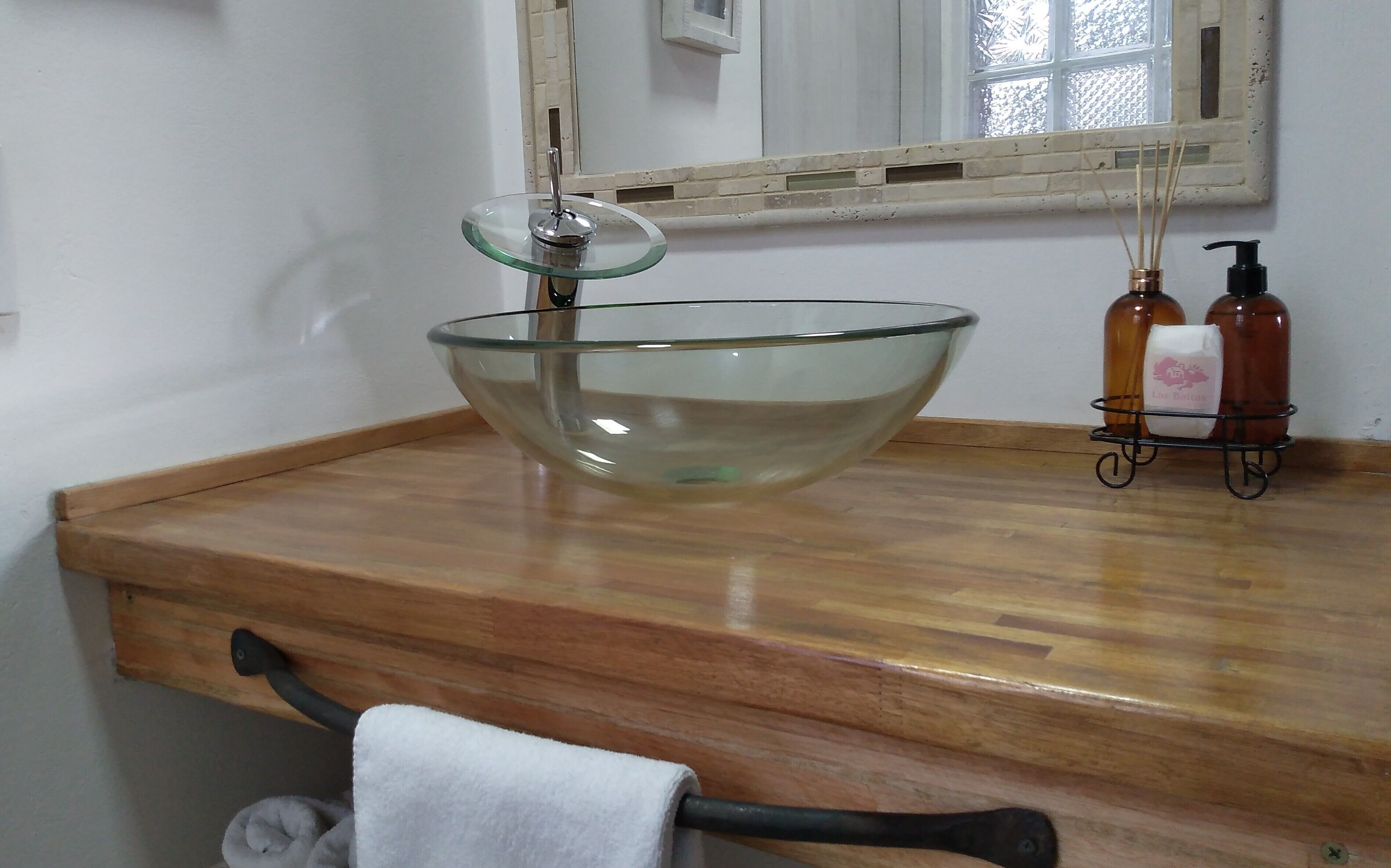 A bathroom with a glass bowl sink, wooden countertop, and a towel rack.
