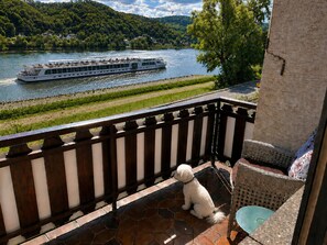 Ein Balkon mit Hund, mit Blick auf einen Fluss und ein Boot.