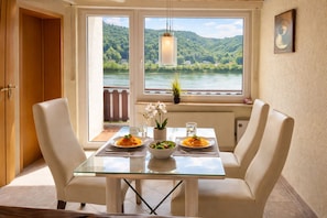 A dining area with a glass table, white chairs, and a view of a lake and forest.