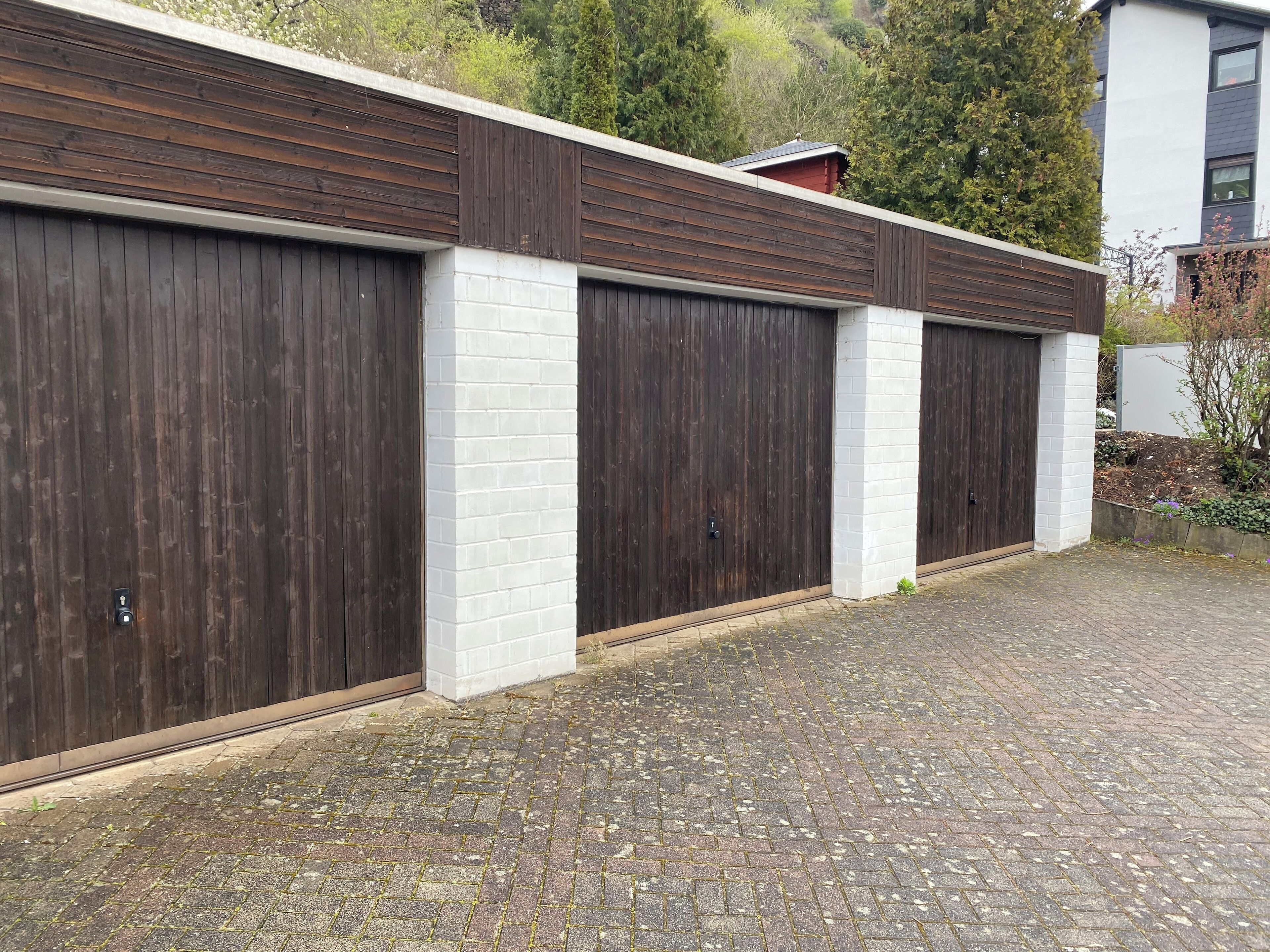 Een modern gebouw met drie grote garage deuren, witte bakstenen pilaren en een verharde oprit.
