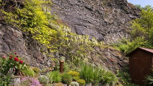 Un jardín con césped, un muro de piedra y una caseta de madera.