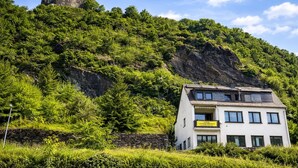 Un castillo en una colina, un edificio moderno con balcón y abundante vegetación.
