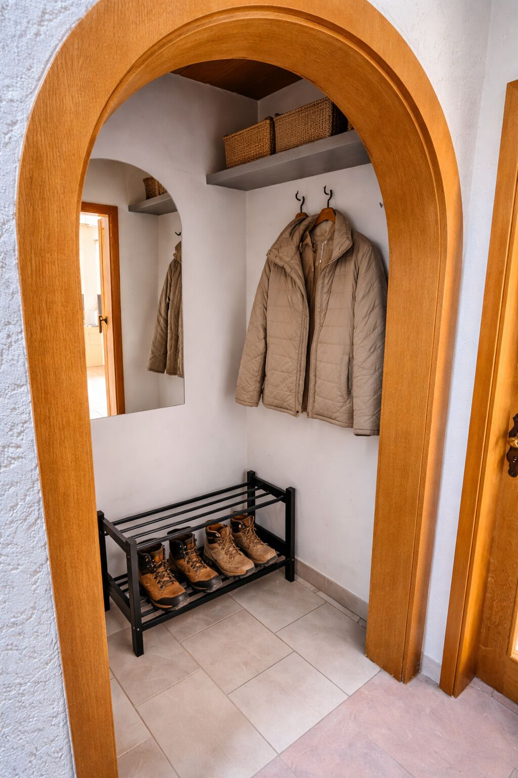 Un pasillo con un arco de madera, un banco con zapatos y un perchero con chaquetas.