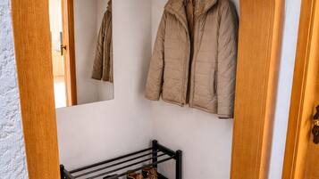 Un pasillo con un arco de madera, un banco con zapatos y un perchero con chaquetas.