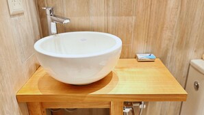 Ein Badezimmer mit einem weißen Waschbecken auf einem Holzsockel, einem Chromarmaturen und einer kleinen Schachtel auf der Ablagefläche.