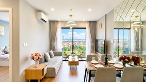 A modern living room with a sofa, dining table, and a city view. - 1 Bedroom Vinhomes Smart City (Hanoi)