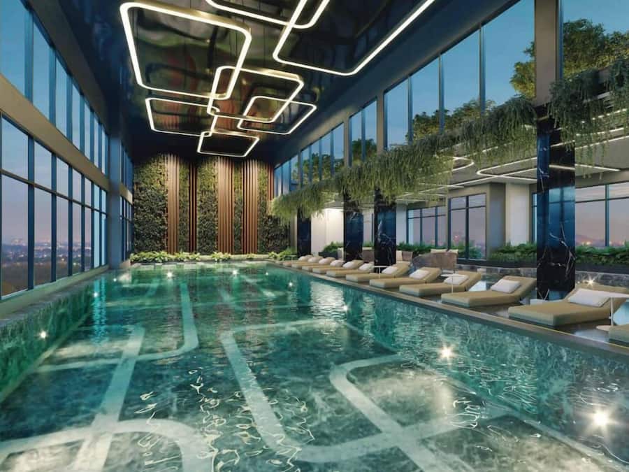 An indoor swimming pool with clear water, surrounded by large windows and lounge areas with cushions.