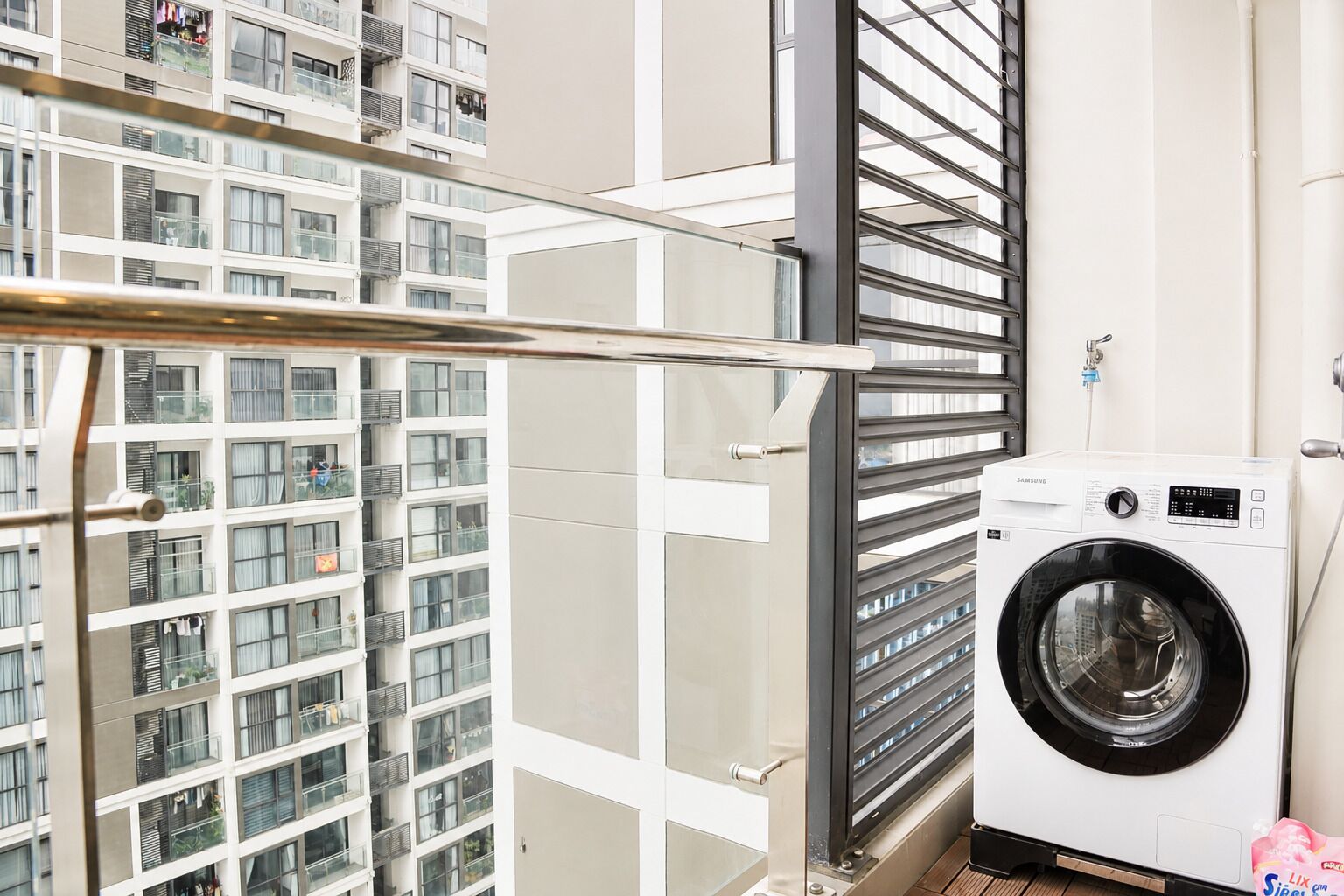 A modern apartment with a balcony, a washing machine, and a view of a high-rise building.