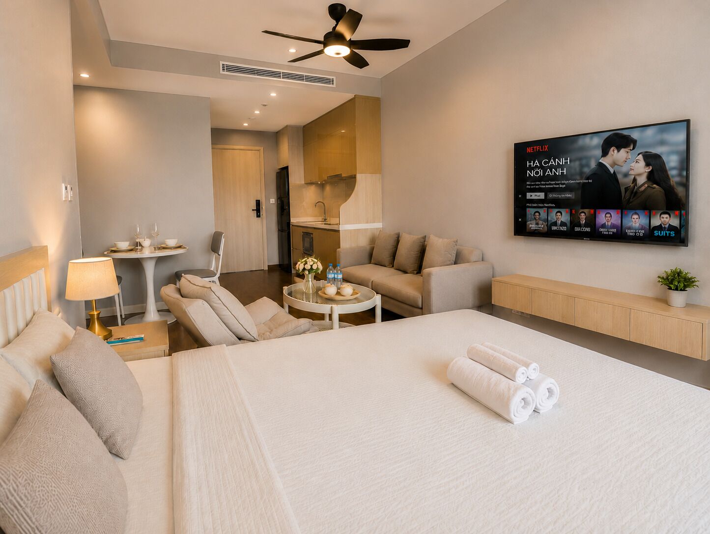 A hotel room with a bed, a sofa, a dining table, a TV, and a kitchenette.