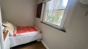 Una camera piccola con un letto singolo, una finestra con tende e un'opera d'arte appesa al muro.
