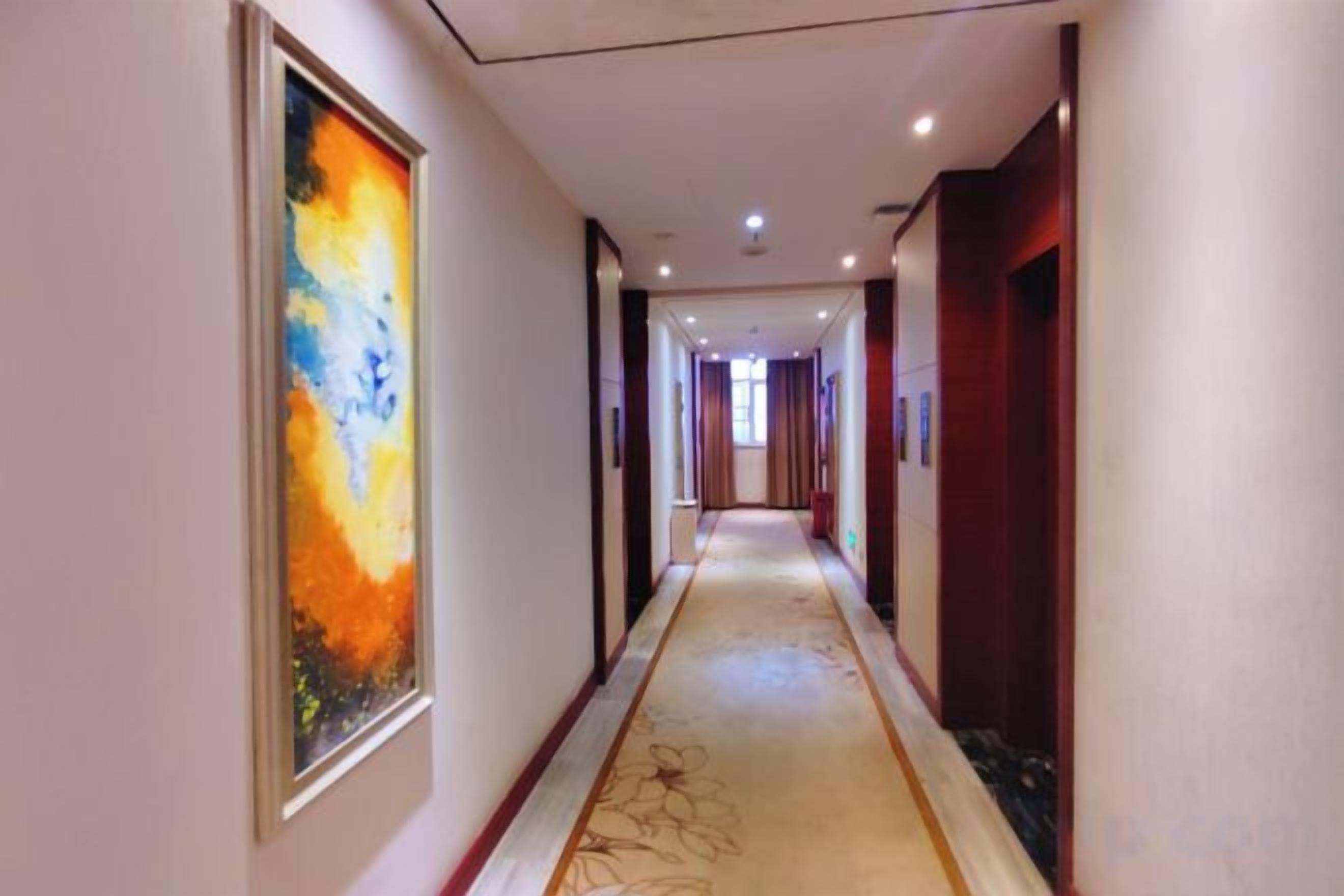 Un pasillo de hotel con piso alfombrado, obras de arte enmarcadas en las paredes y puertas que dan a las habitaciones.