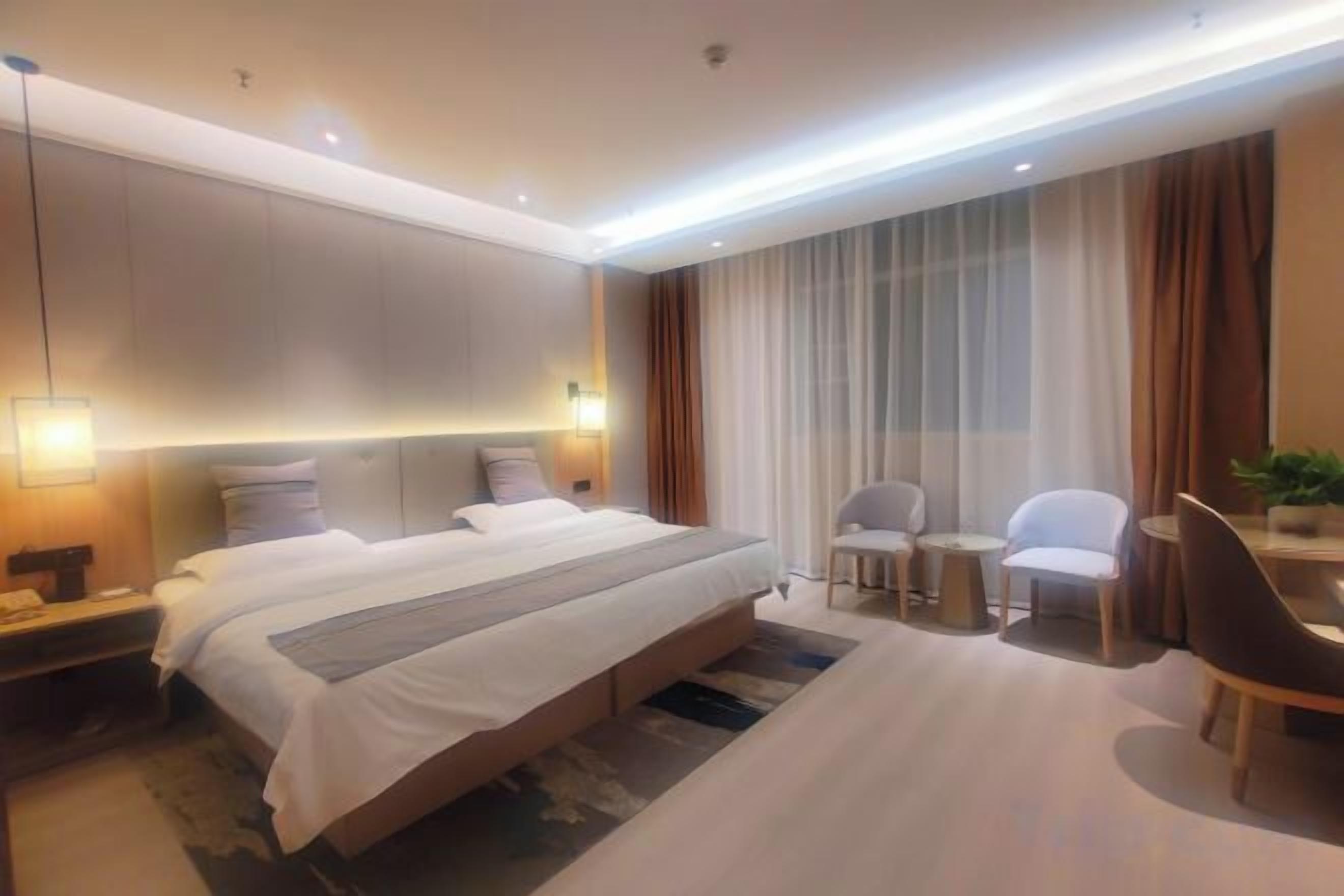 A modern hotel room with a large bed, bedside tables, a desk with a chair, and a small table with two chairs.