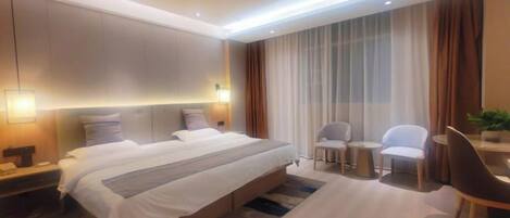 A modern hotel room with a large bed, bedside tables, a desk with a chair, and a small table with two chairs.