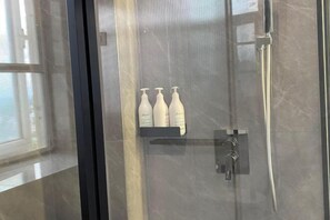A glass-enclosed shower area with a control panel and three bottles of shampoo on a shelf. - Shengda Hotel (Guangshan)