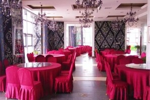 A banquet hall with round tables and chairs, large windows, and chandeliers. - Shengda Hotel (Guangshan)