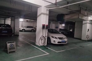 A parking garage with multiple cars, including a white sedan and a black SUV, parked near charging stations. - Shengda Hotel (Guangshan)