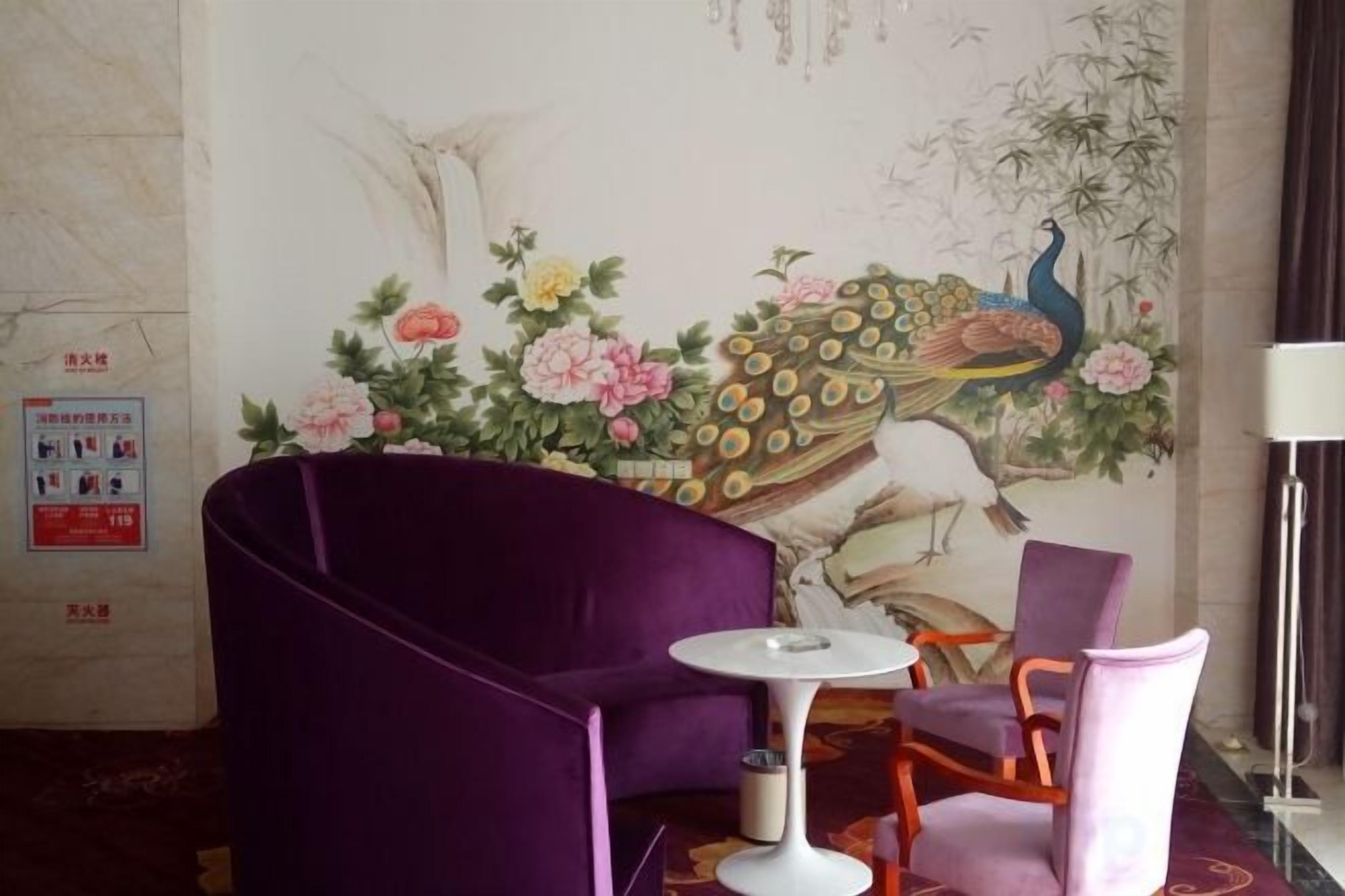 A room with a purple sofa, a small round table, and a chair. There is a mural on the wall depicting birds and flowers.