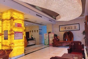 A hotel lobby with a reception desk, a large illuminated pillar, and a traditional Chinese decorative piece. - Shengda Hotel (Guangshan)