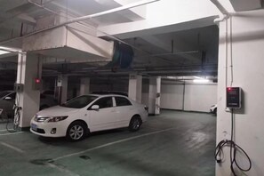 A white car parked in an underground parking garage with visible structural elements and a control panel on the wall. - Shengda Hotel (Guangshan)