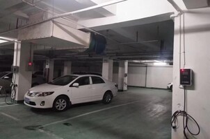 Un auto blanco estacionado en un estacionamiento subterráneo con elementos estructurales visibles y un panel de control en la pared.