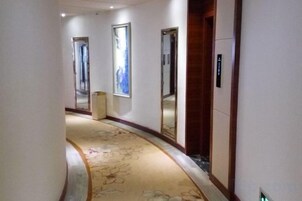 Un pasillo de hotel con piso alfombrado, una puerta de madera y un espejo en la pared.