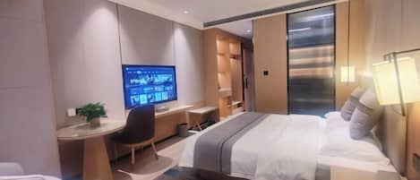 A modern hotel room with a large bed, a desk with a computer, a chair, and a TV.