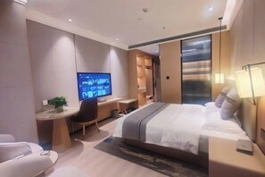 Una habitación de hotel moderna con una cama grande, un escritorio con computadora, una silla y un televisor.