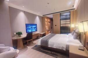 A modern hotel room with a large bed, a desk with a computer, a chair, and a TV.