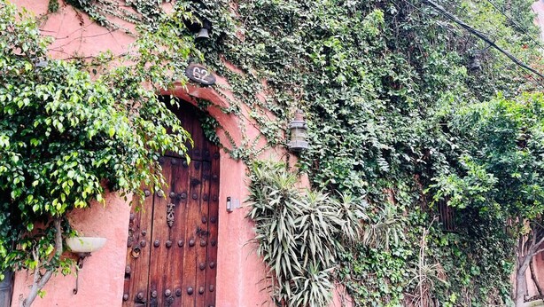 Un edificio rústico con puerta de madera, una campana y un farol.