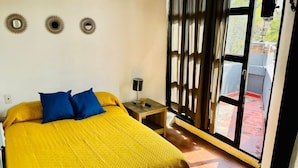 Una habitación con cama, mesita de noche y ventana con cortinas.