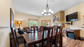 A spacious dining area with a wooden table and chairs, a chandelier, and a television mounted on the wall. - Al8123-2 (Keystone)