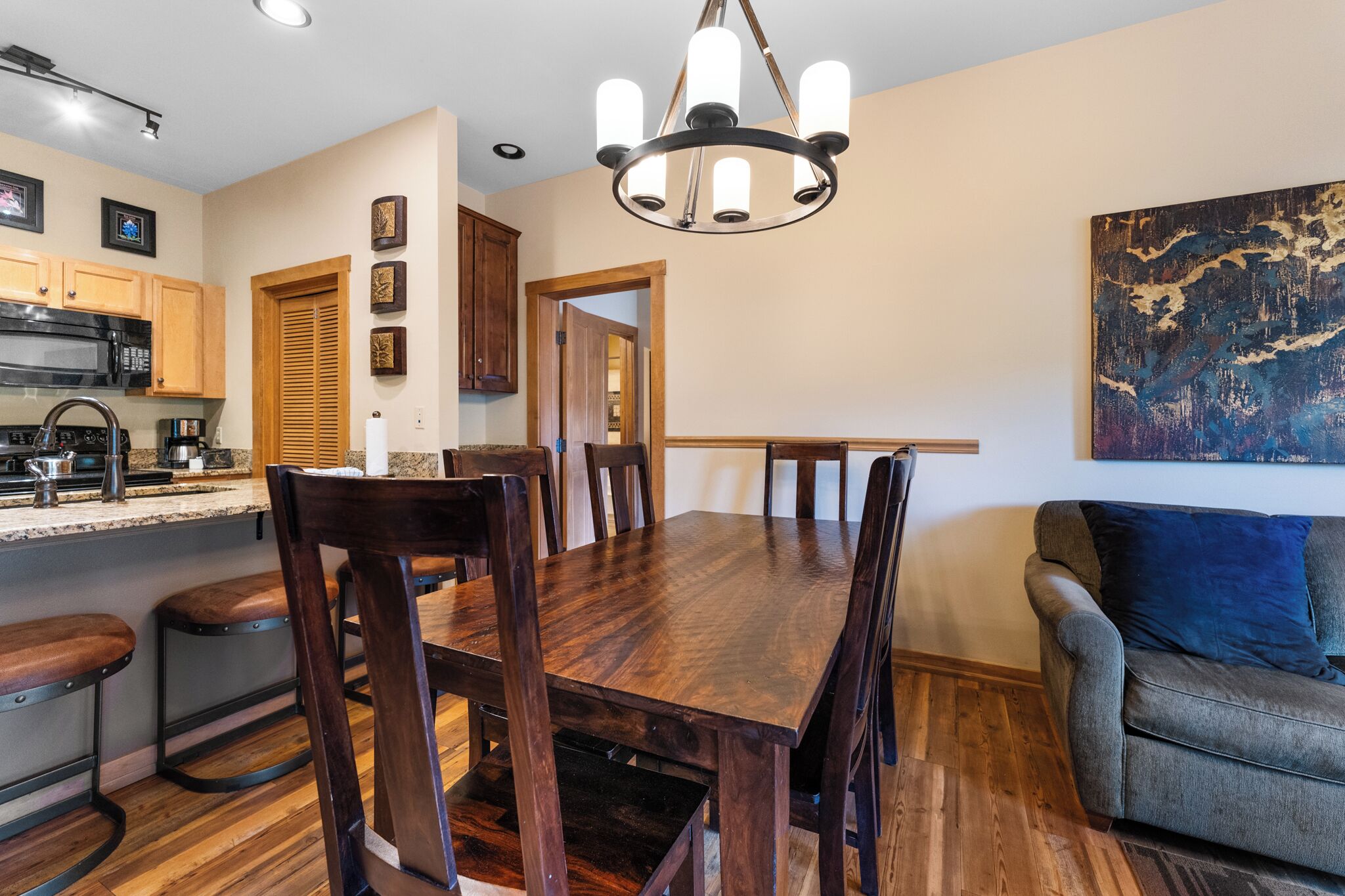 A dining area with a wooden table and chairs, a kitchen with a microwave and stove, and a painting on the wall.