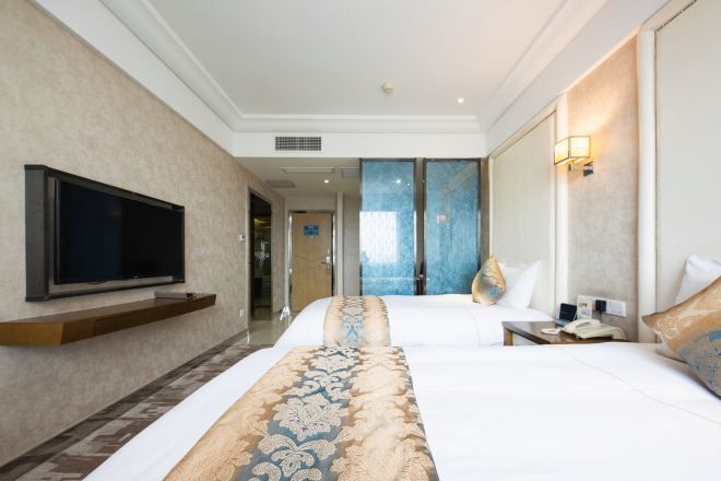 A hotel room with a large bed, a flat-screen TV, a bedside table with a phone, and a wall-mounted TV.