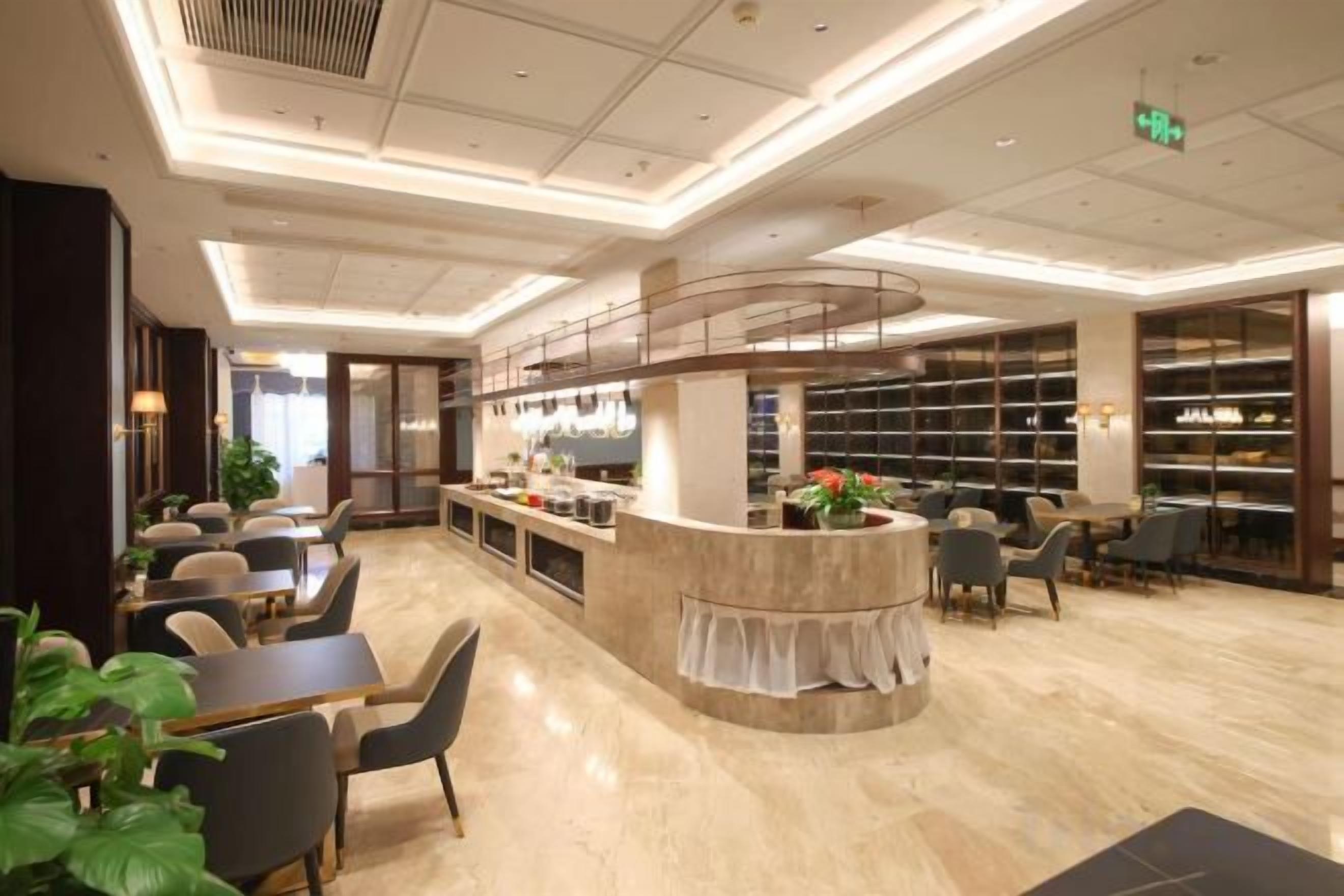 A modern hotel lobby with a central bar area, seating arrangements, and a large bookshelf.